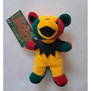 May include: A small, yellow, green, red, and black plush bear with a black mouth and a tag that says "The Grateful Dead" on it.