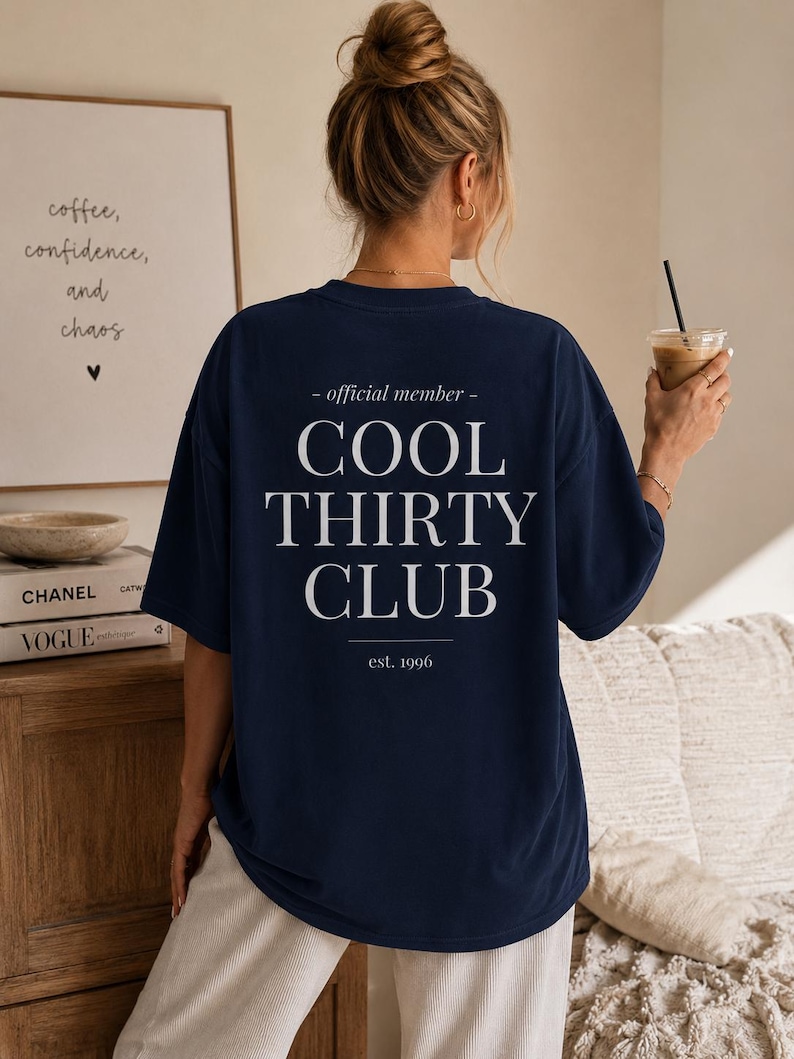 May include: A navy blue short-sleeve t-shirt featuring white text on the back that reads: - official member - COOL THIRTY CLUB est. 1996. The shirt has a crew neckline and a loose, relaxed fit, displaying the back design clearly.