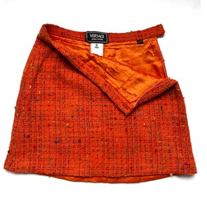 Puede incluir: Minifalda de tweed naranja con dise&ntilde;o envolvente. La falda presenta una tela texturizada con motas de color y un forro de sat&eacute;n naranja. Se ve una etiqueta negra con texto blanco.
