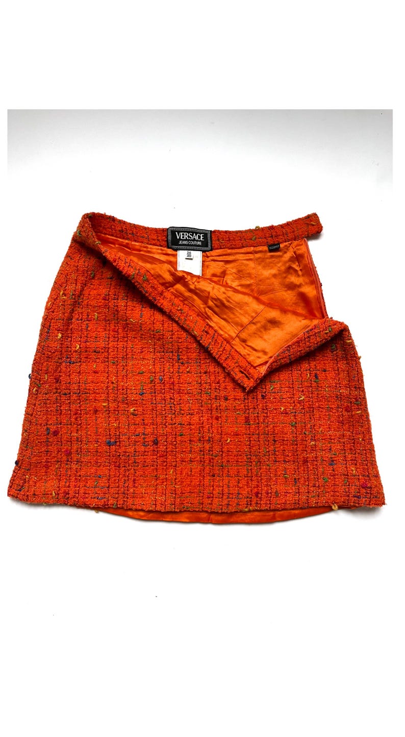 Puede incluir: Minifalda de tweed naranja con dise&ntilde;o envolvente. La falda presenta una tela texturizada con motas de color y un forro de sat&eacute;n naranja. Se ve una etiqueta negra con texto blanco.