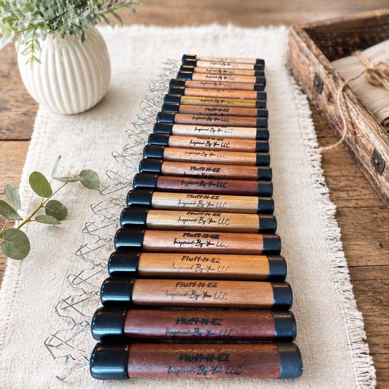 May include: A collection of wooden tools with black end caps arranged in a row. Each tool features the text Fluff-N-EZ and Inspired By You LLC printed on the surface. The tools vary in wood grain color from light tan to dark brown tones.