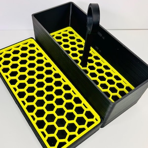 May include: Black rectangular storage container with a yellow honeycomb pattern insert and a handle. The lid is open, revealing the interior. The container is made of a textured material.