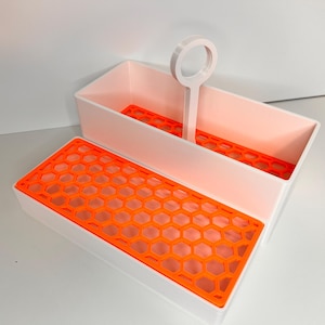 May include: A white rectangular organizer with an orange honeycomb-patterned tray and a matching orange insert. The organizer has a handle and is designed to hold items. The design is modern and functional.