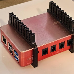 May include: A red and black computer with a black plastic cooling fan attached to the top. The computer has a DC 12V output and several ports on the back.