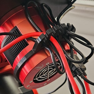 Puede incluir: Primer plano de un brazo robótico rojo con cables negros y un motor rojo. El brazo está unido a una pared blanca.