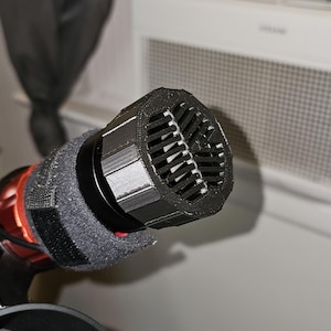 Op de afbeelding: Close-up van een zwarte microfoon met een schuimwindkap en een zwart gaasrooster.