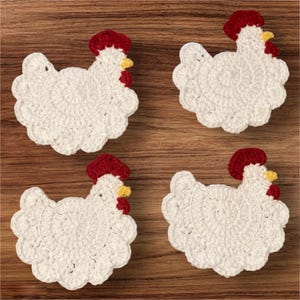 May include: Four white crochet chicken-shaped coasters with red combs and yellow beaks are arranged on a wooden surface. The coasters are handmade and have a scalloped edge. The overall theme is farmhouse decor.