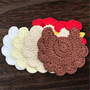 May include: A set of four layered crochet coasters shaped like chickens, featuring scalloped edges. The coasters are colored in white, pale yellow, beige, and brown, each topped with a bright red crochet comb and a small yellow beak detail.