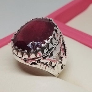 Puede incluir: Un anillo de plata con un diseño adornado y una gran piedra preciosa de color rojo oscuro de forma ovalada.