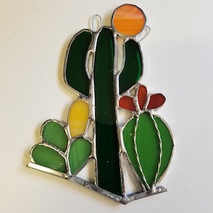 May include: A stained glass cactus with green, yellow, orange, and red glass pieces. The cactus is surrounded by smaller green cacti.