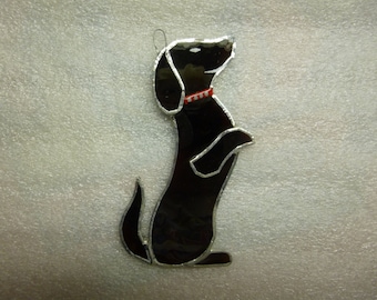 May include: Black stained glass silhouette of a dog standing on its hind legs, wearing a red and white collar.