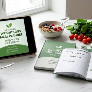 Pode incluir: Um tablet exibindo The Complete Weight Loss Meal Planner, um livro correspondente, uma agenda aberta com uma caneta verde, uma tigela de aveia com frutas, uma garrafa de água e vegetais frescos incluindo espinafre, tomates e pepino.