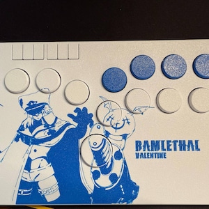 May include: A rectangular white arcade controller featuring a blue graphic of the character Ramlethal Valentine with the text "RAMLETHAL VALENTINE" printed in blue. The device includes several white and blue circular buttons and four small rectangular buttons.