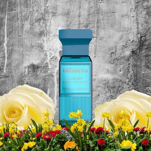 May include: A turquoise perfume bottle with a blue cap, labeled "olfazeta LUXURY Extrait de Parfum 50 mL (1.69 fl oz)". The bottle is set against a gray and white background, with yellow roses and colorful flowers in the foreground.
