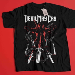 Peut inclure: T-shirt noir avec un motif blanc d'un personnage du jeu vidéo Devil May Cry. Le motif représente le personnage debout avec des épées dans les mains et le texte "Devil May Cry" au-dessus.