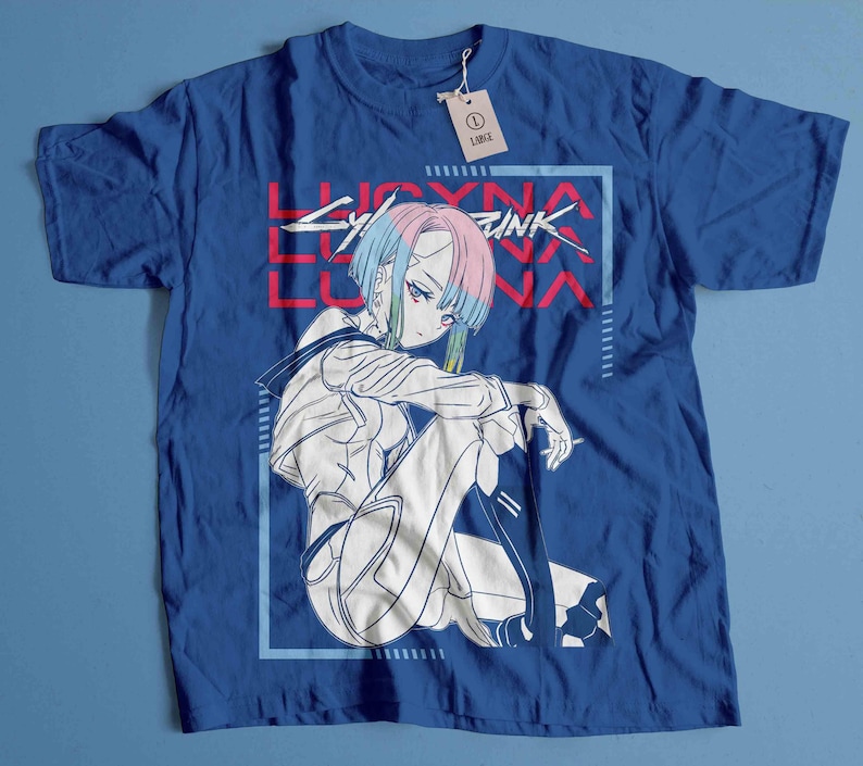 Peut inclure: T-shirt bleu roi avec une illustration de style anime. Le motif pr&eacute;sente un personnage aux cheveux bleus, roses et verts, et le texte "LUCYNA CYBERPUNK" en rouge et blanc. Une &eacute;tiquette indique la taille L.