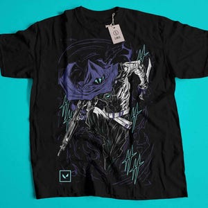 Peut inclure: T-shirt noir avec une illustration détaillée d'un personnage encapuchonné tenant une arme. Le design utilise des touches de violet et de turquoise sur un fond sombre. Une étiquette indique "LARGE".