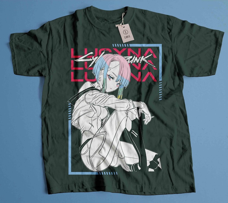 Peut inclure: T-shirt vert fonc&eacute; avec une illustration de style anime. Le motif pr&eacute;sente un personnage aux cheveux bleus et roses, le texte "LUCYNA LUNA" en rose et un cadre rectangulaire bleu. Une &eacute;tiquette indique "LARGE".