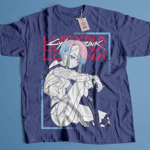 Peut inclure: T-shirt bleu marine avec un dessin d'un personnage d'anime assis aux cheveux bleus et roses, dans un cadre rectangulaire bleu. Le texte "LUCYNA LUNA CYBERPUNK" est imprim&eacute; en rouge. Une &eacute;tiquette indique "LARGE".