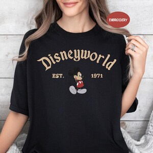 A woman wearing a black t-shirt with the text "Disneyworld EST. 1971" and an embroidered image of Mickey Mouse.