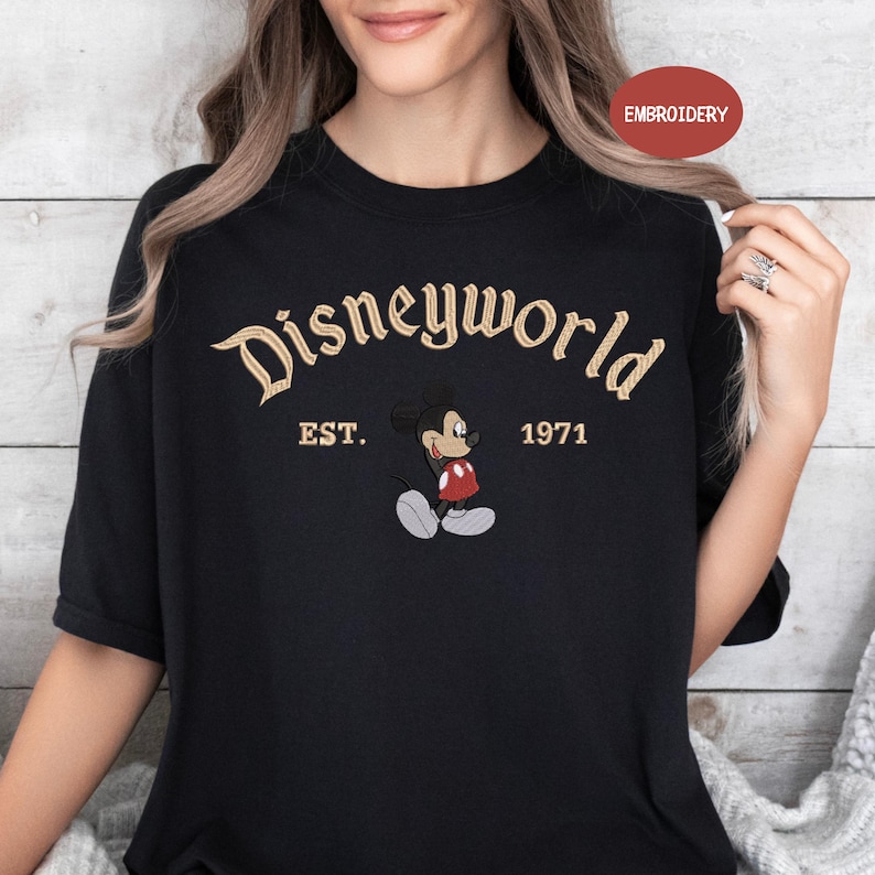 A woman wearing a black t-shirt with the text "Disneyworld EST. 1971" and an embroidered image of Mickey Mouse.