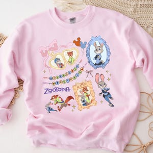 A pink sweatshirt with a cartoon character design featuring various animals, including a rabbit, fox, and dog, along with the text "Zootopia" and a heart-shaped frame.