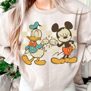 A person wearing a white sweatshirt with a graphic of Mickey Mouse and Donald Duck.