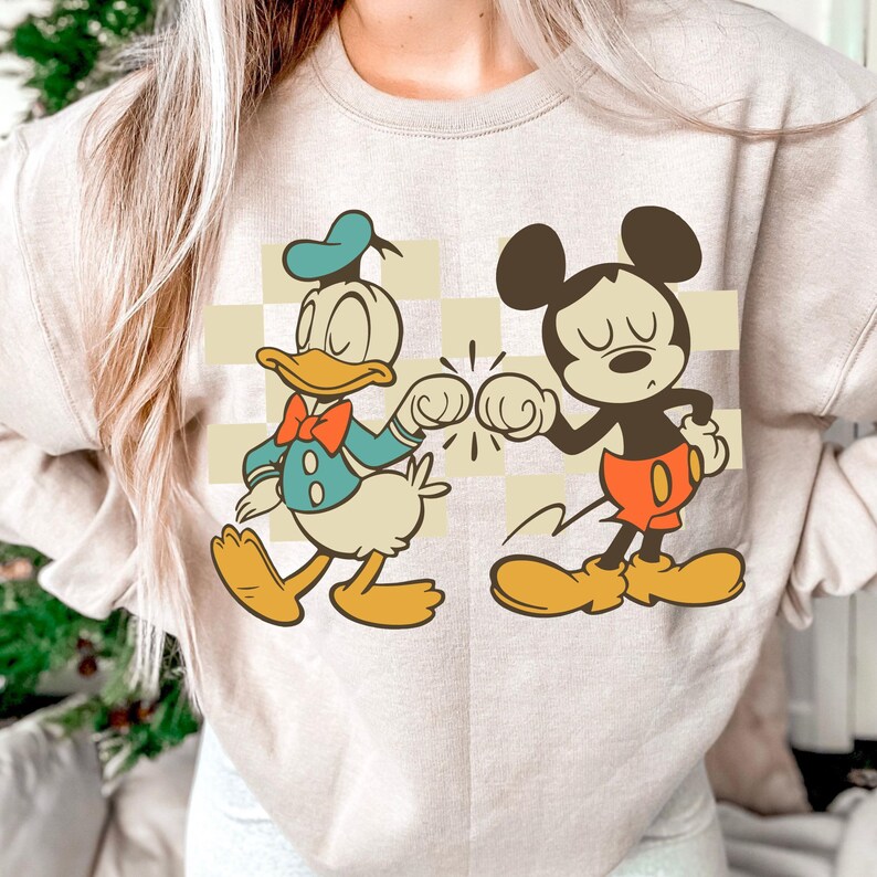 A person wearing a white sweatshirt with a graphic of Mickey Mouse and Donald Duck.