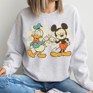 A woman wearing a gray sweatshirt with a graphic of Mickey Mouse and Donald Duck.
