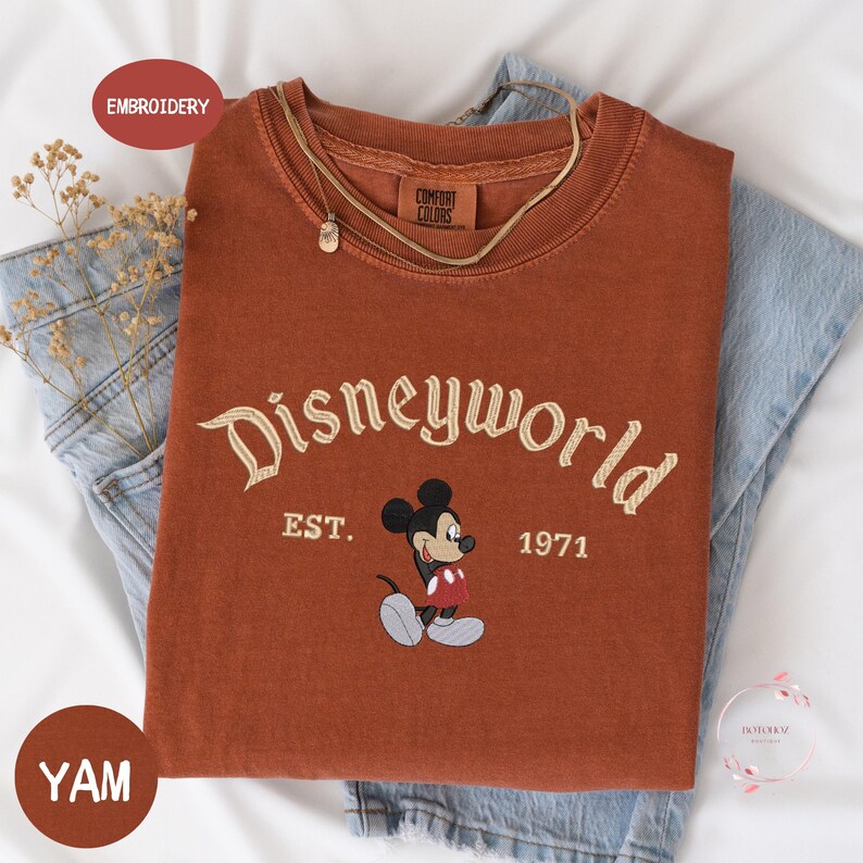 a red t-shirt with the text "Disneyworld EST. 1971" and a Mickey Mouse graphic, along with a denim jacket and some flowers.