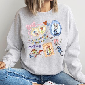 A gray sweatshirt with a colorful graphic design featuring various cartoon animal characters, including a rabbit, fox, and dog, along with a mirror and a heart.
