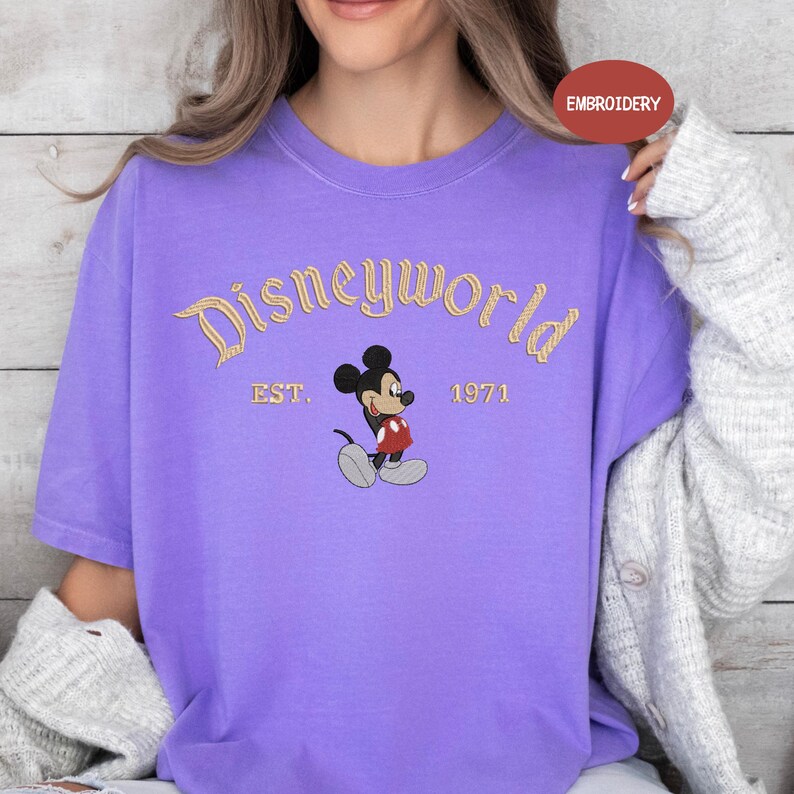 A woman wearing a purple t-shirt with a Mickey Mouse design and text that says "Disneyworld EST. 1971".