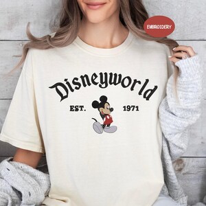A woman wearing a white t-shirt with the text "Disneyworld EST. 1971" and a Mickey Mouse graphic.