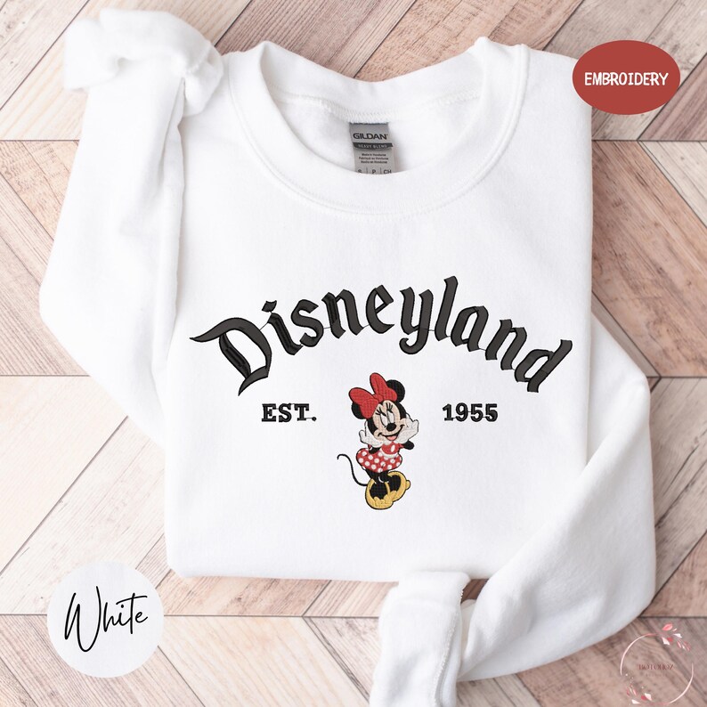 A white sweatshirt with the text "Disneyland" and "EST. 1955" printed on it, along with a Minnie Mouse character.