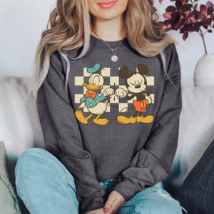 A woman wearing a gray sweatshirt with a graphic of Mickey Mouse and Donald Duck.