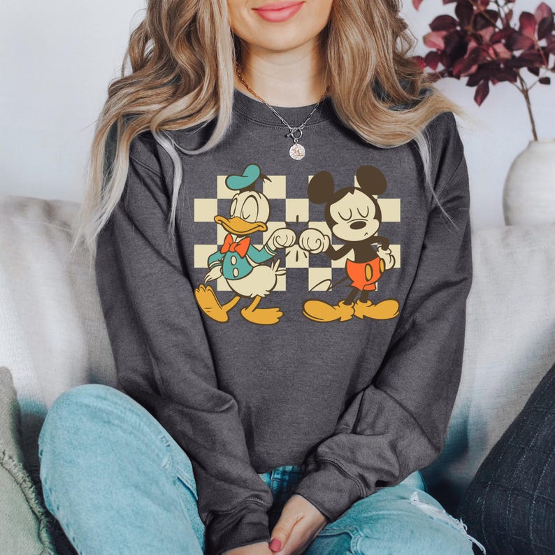 A woman wearing a gray sweatshirt with a graphic of Mickey Mouse and Donald Duck.