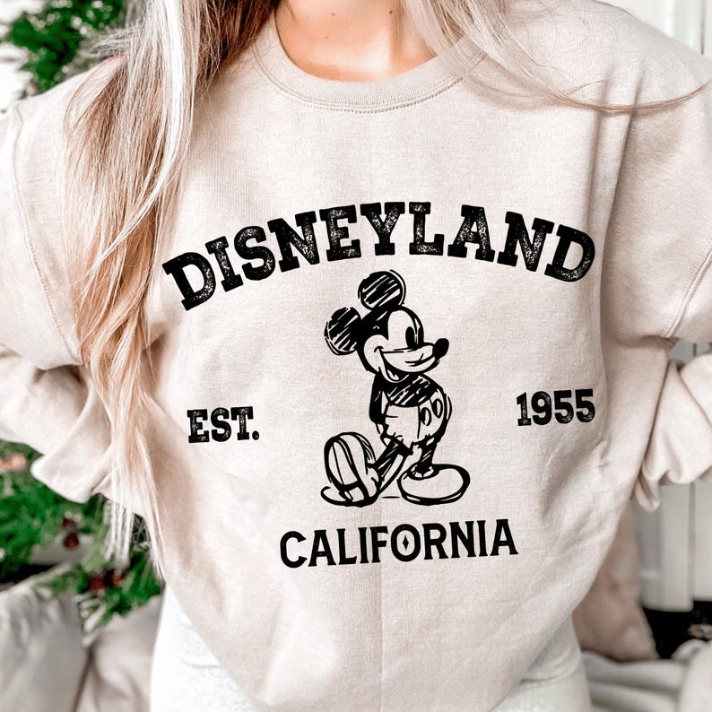A person wearing a white sweatshirt with a graphic of Mickey Mouse and text that says "Disneyland Est. 1955 California".