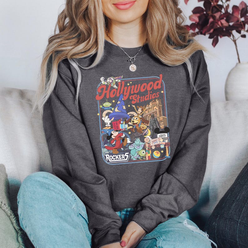 A woman wearing a gray sweatshirt with a graphic of Disney characters and the text "Hollywood Studios" is sitting on a couch.