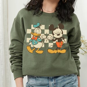 A woman wearing a green sweatshirt with a graphic of Mickey Mouse and Donald Duck on it.