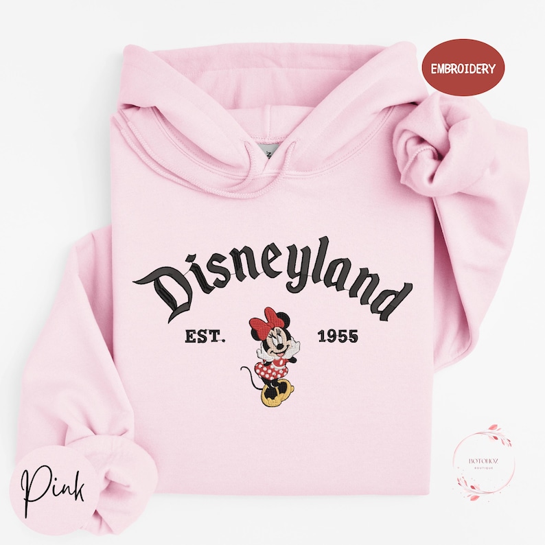 A pink hoodie with the text "Disneyland EST. 1955" and a Minnie Mouse graphic, indicating it is a souvenir or merchandise item from the Disney theme park.