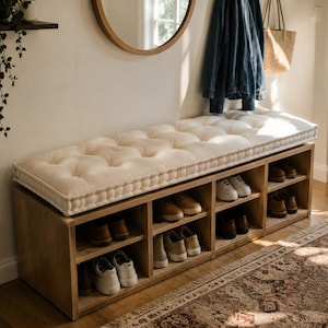 May include: A rectangular wooden shoe storage bench featuring a tufted off-white cushion on top. The base consists of eight open cubby compartments, each containing various pairs of sneakers and dress shoes in shades of white, tan, and brown.