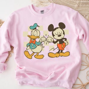 A pink sweatshirt with a cartoon image of Mickey Mouse and Donald Duck.