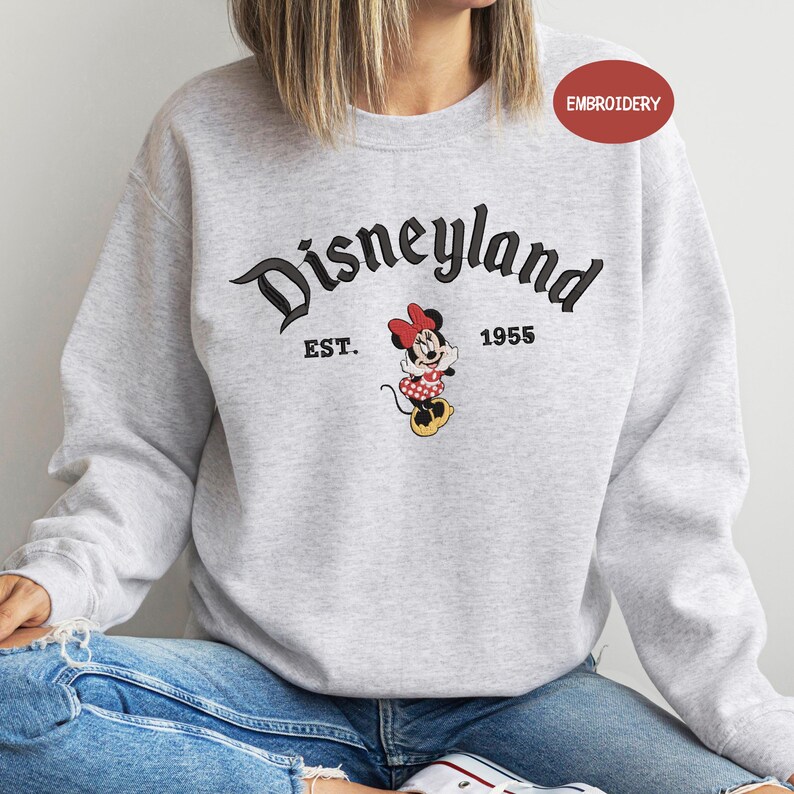 A person wearing a gray sweatshirt with the text "Disneyland EST. 1955" and a Minnie Mouse graphic printed on it.