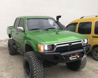May include: A bright green pickup truck with a black front bumper and a large black snorkel. The truck has large tires and is lifted.