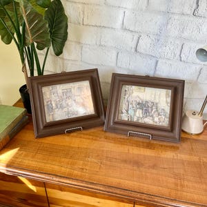 May include: Two framed illustrations of people in a street scene. The frames are brown wood with a simple design. The illustrations are in a vintage style and feature people in period clothing.