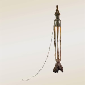 May include: A hanging light fixture featuring a tall, cylindrical macrame cage made of tan cord. The structure is suspended by a metal chain and terminates at the bottom in a dark, textured piece of natural driftwood that anchors the design.