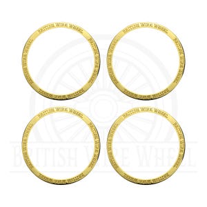 May include: Four gold-colored circular rings with the text "BRITISH WIRE WHEEL" engraved around the outer edge. The rings are arranged in a square formation against a white background, suggesting automotive parts or accessories.
