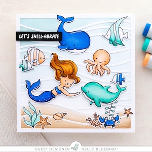 May include: A white card with a blue, green, and orange underwater scene. The card features a mermaid, a whale, a dolphin, an octopus, a crab, and fish. The text "Let's Shell-abrate" is written on the card.