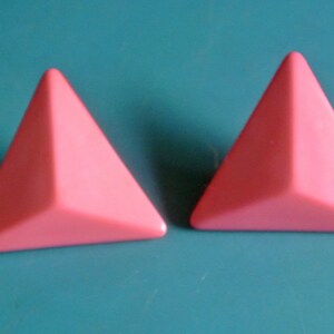 Pode incluir: Um par de brincos triangulares cor de rosa.