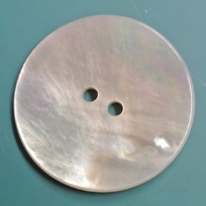Puede incluir: Un botón blanco de nácar con dos agujeros.